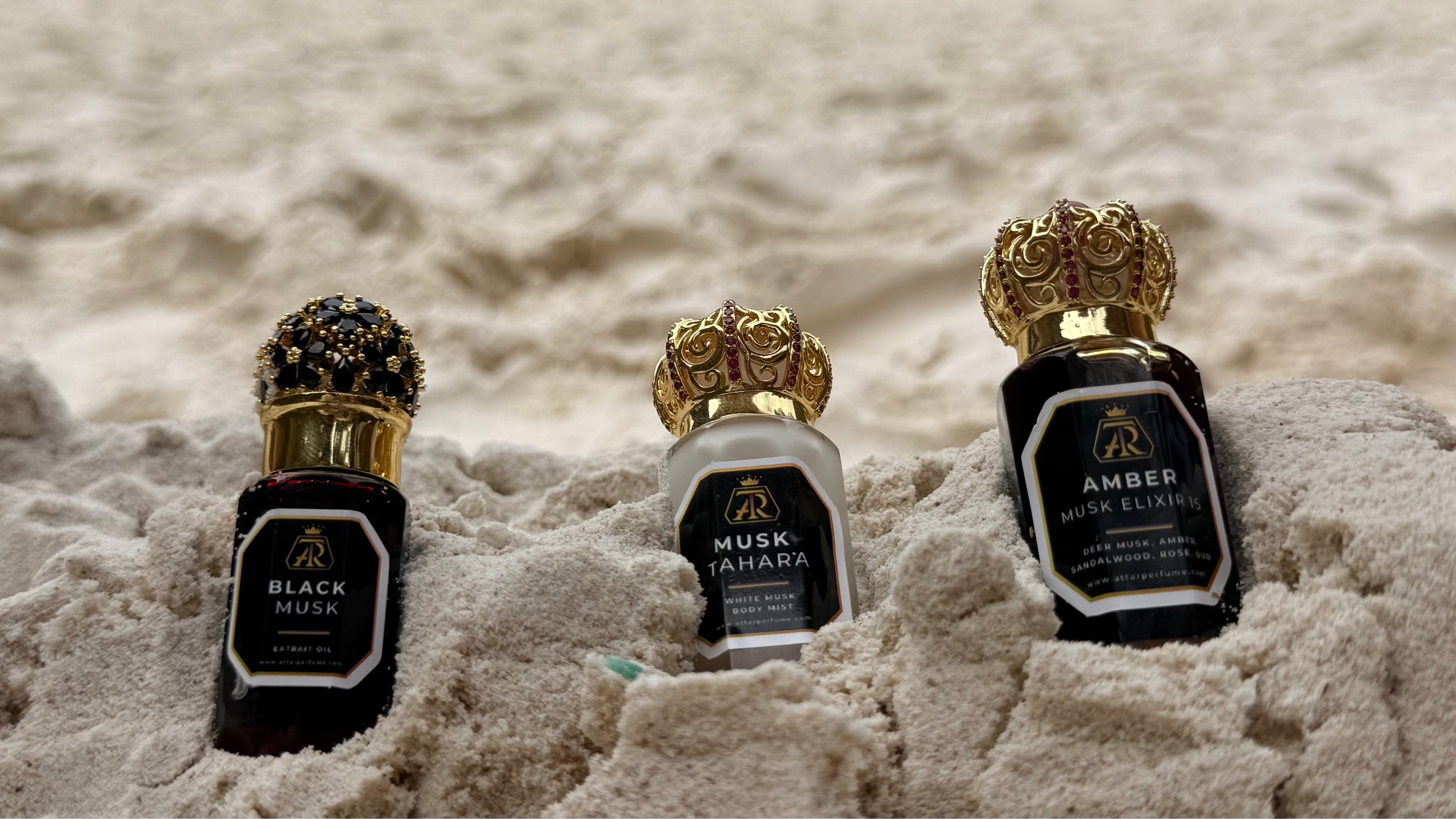 Three perfume bottles on a sandy beach with people in the background.