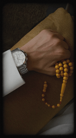 Hand wearing a watch with a string of yellow beads on a brown surface