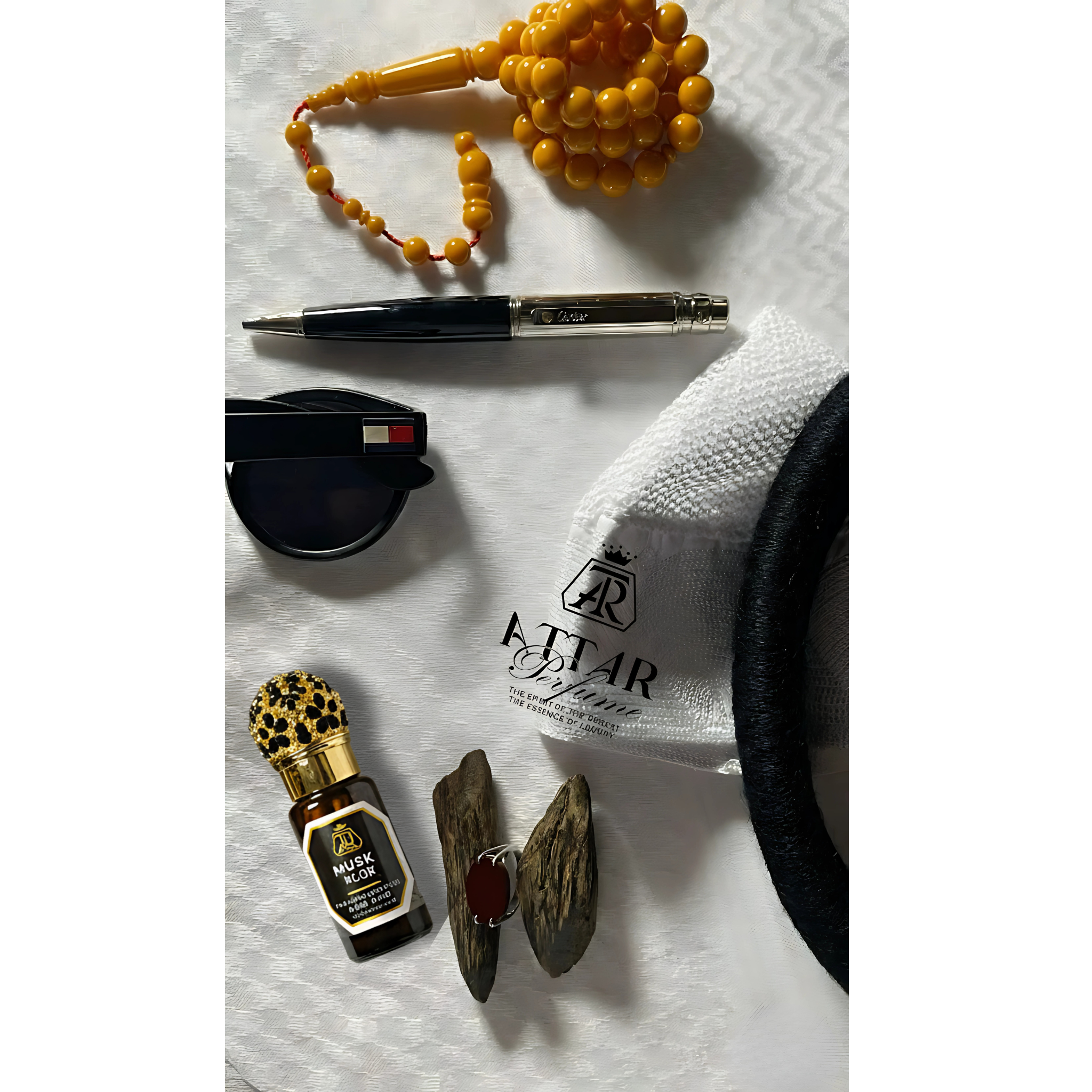 Collection of items including a pen, yellow beads, a bottle, and a piece of jewelry on a white surface with 'Attar' branding.
